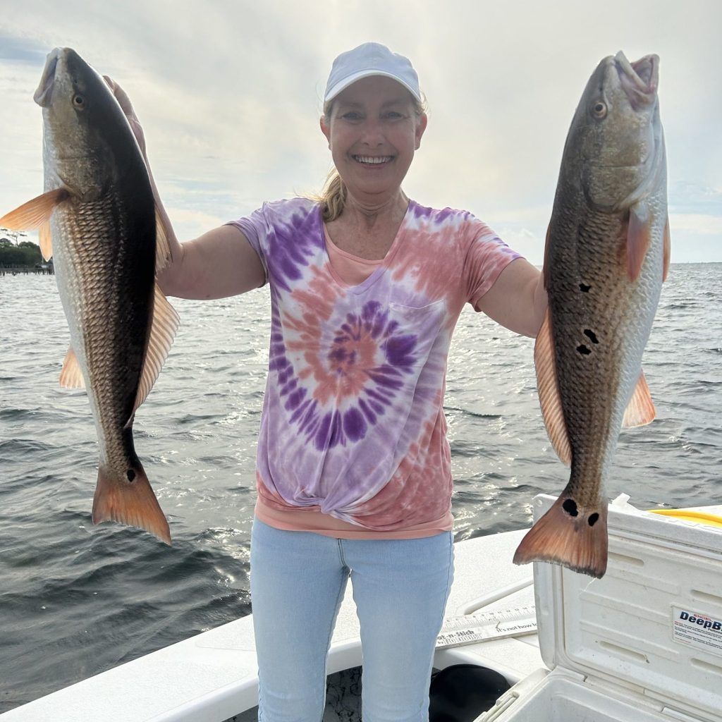 Angler holding two redfish caught on a cool-weather inshore charter near Navarre Beach
