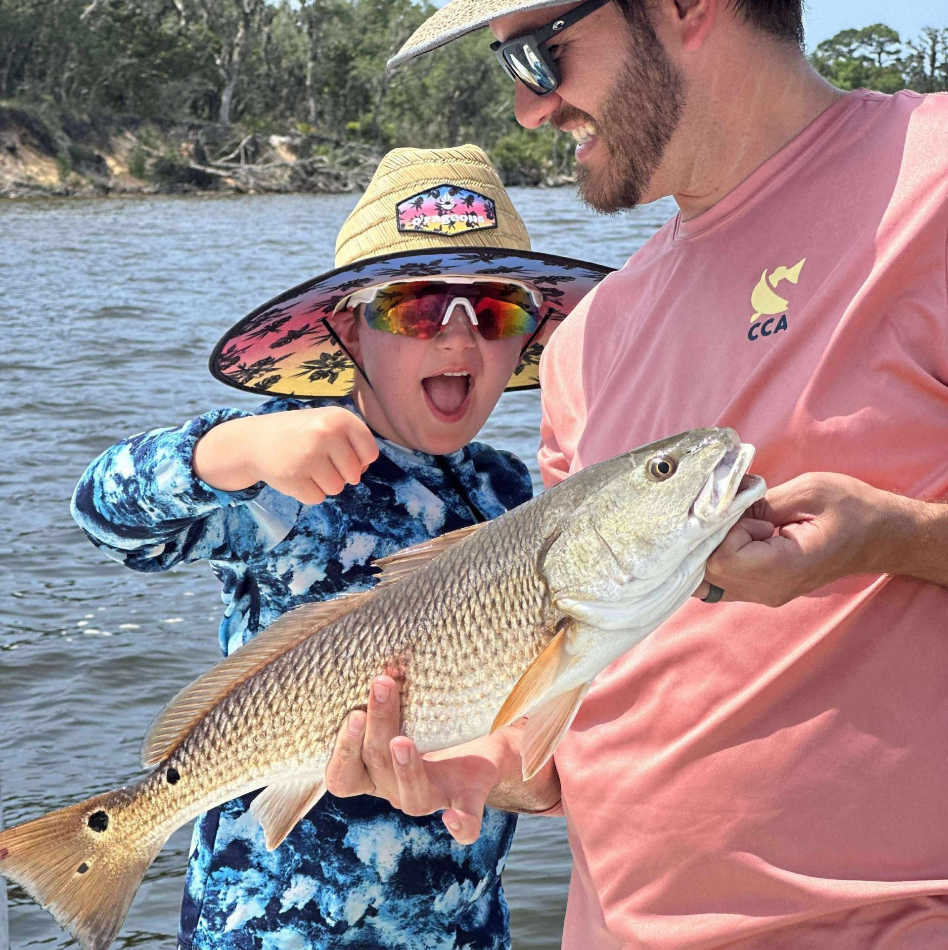 Gulf Breeze fishing charter guest holding speckled trout on calm water with redfish tail in background